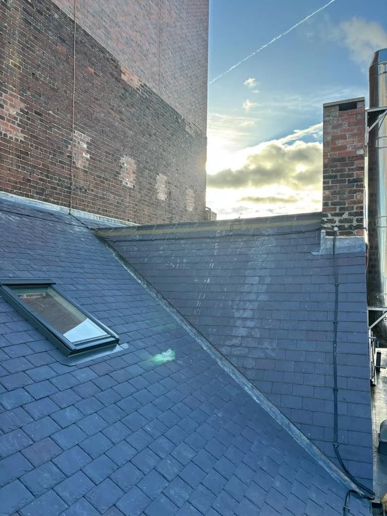 Completed Welsh slate roof at Leeds Grand Theatre against a blue sky, with new ridges, leadwork and chimney after the heritage refurbishment.