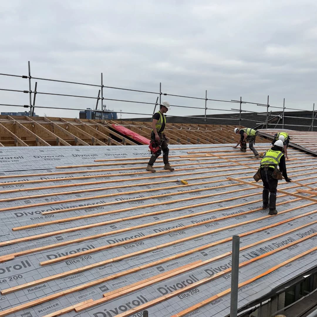 Evenii operatives in branded hi-vis installing timber battens over Divoroll Elite 200 underlay on a commercial pitched roof — about Evenii