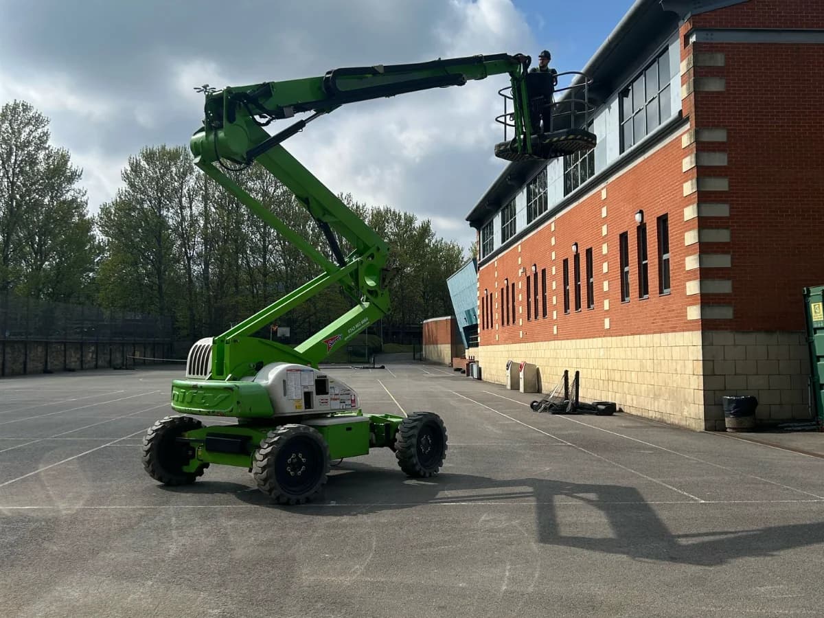 Articulated boom platform reaching a two-storey red brick commercial building roof under blue sky